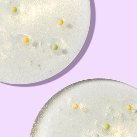 Close up of circles of skin brightening cleanser with yellow beads in front of light purple background